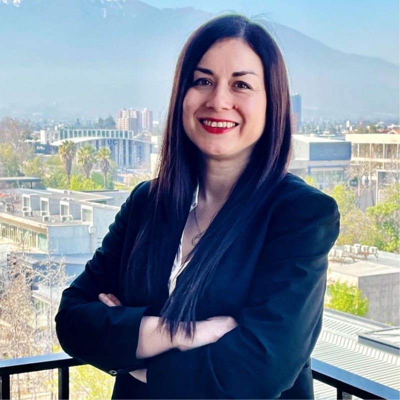A woman standing with her arms crossed. There is an urban landscape in the background.